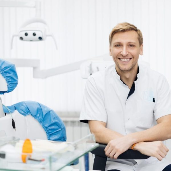 Portrait of a positive young male dentist in uniform at the dental office